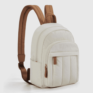 Home A side view of the beige quilted mini backpack showing its vertical stitching pattern and brown handle attachments.