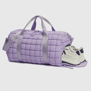 Home A light purple quilted duffle bag with a side shoe pocket open revealing a pair of white sneakers.