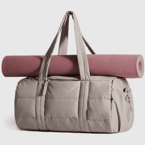 A beige quilted duffel bag with a pink yoga mat strapped horizontally across the top exterior