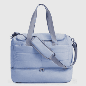 A light blue quilted travel duffel bag with a bottom shoe compartment and a detachable padded strap
